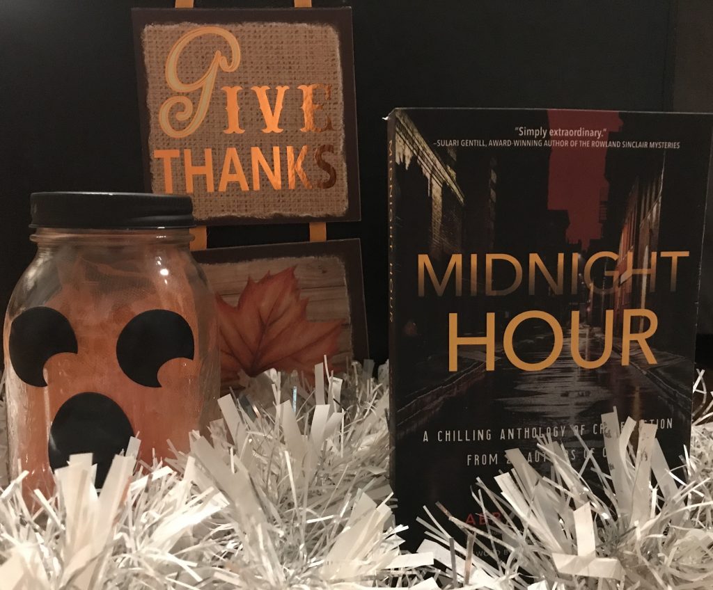 MIDNIGHT HOUR anthology next to "Give Thanks" sign and a jar with a jack-o-lantern face and surrounded by a white tinsel garland