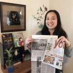 Asian American author Jennifer J. Chow holding up newspaper article in front of desk and books