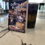 Bubble tea in colors of purple and gold to match Death by Bubble Tea mystery novel next to it
